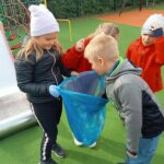 Dzieci sprzątają plac zabaw trzymając worek na śmieci