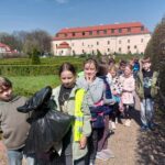 Uczniowie klasy drugiej dumnie trzymają worki ze śmieciami po zakończonym sprzątaniu. Dzieci są w Ogrodach Bony, w tle widać Zamek