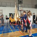 Uczniowie stoją na baczność, sztandar jest pochylony w trakcie śpiewania hymnu Polski