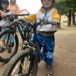 Na zdjęciu widać chłopca- zawodnika wyścigu rowerowego dla dzieci. Chłopiec dumnie prezentuje swój rower z odblaskami