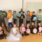 Dzieci stoją i siedzą w dwóch rzędach trzymając balony