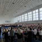 Społeczność szkolna zebrana na sali gimnastycznej śpiewa pieśni patriotyczne