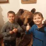 Uśmiechnięci chłopcy stoją przed eksponatem niedźwiedzia