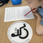Chłopiec siedzi w ławce i próbuje rozkodować litery napisane alfabetem Braille'a