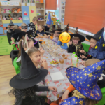 Dzieci w strojach czarodziejów siedzą wokół stołów z poczęstunkiem