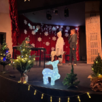 Dzieci występują na scenie, w tle dekoracja świąteczna