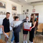Uczniowie klasy 8a wrzucają karty wyborcze do urny trzymanej przez dwie uczennice
