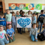 Dzieci trzymają w rękach plakat, na kórym odbite niebieskie dłonie tworzą kształt serca