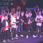 Chłopcy stoją na scenie i grają na gitarach