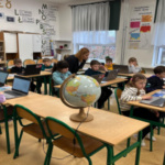 Dzieci siedzą w ławkach i pracują na laptopach