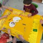 Troje dzieci pracuje przy stoliku, ozdabiają korony
