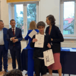 Nagrodzony uczeń pokazuje dyplom, za nim stoją nauczyciele