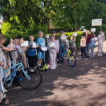 Dzieci stoją na podwórku i pokazują swoje dzienniczki rowerowe
