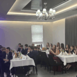Ósmoklasiści siedzą przy dwóch stołach w wieczorowych strojach