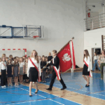 Uczniowie w Poczcie Sztandarowym wchodzą na salę gimnastyczną