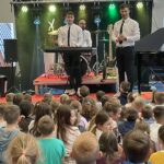 dwóch mężczyzn stoi na scenie, jeden tłumaczy jak zbudowany jest keyboard a drugi mężczyzna gra na instrumencie