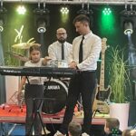 dwóch mężczyzn stoi na scenie, z lewej strony stoi dziewczynka, która gra na instrumenie