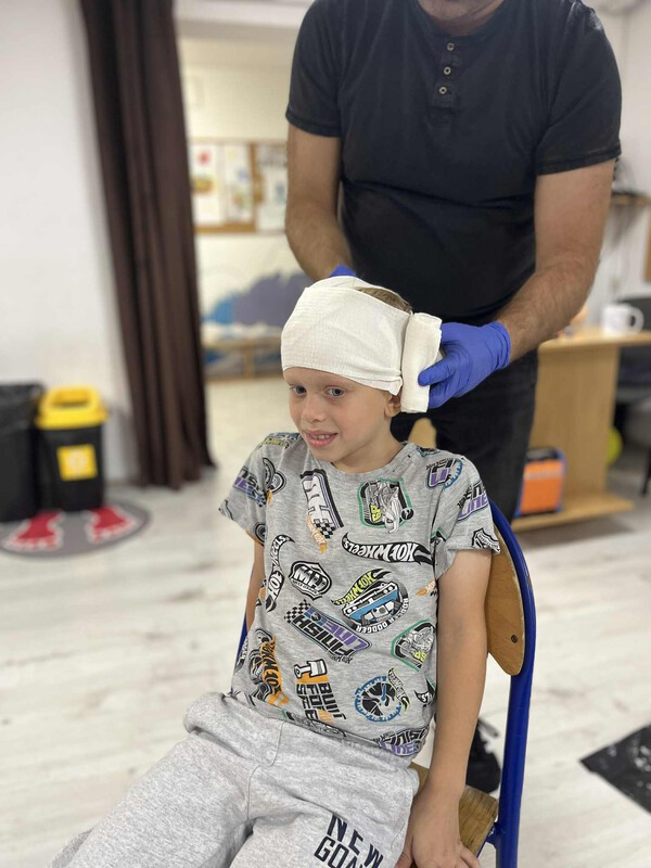 Na zdjęciu widać chłopca na którego głowie demonstrowany jest opatrunek tzw. czepiec.