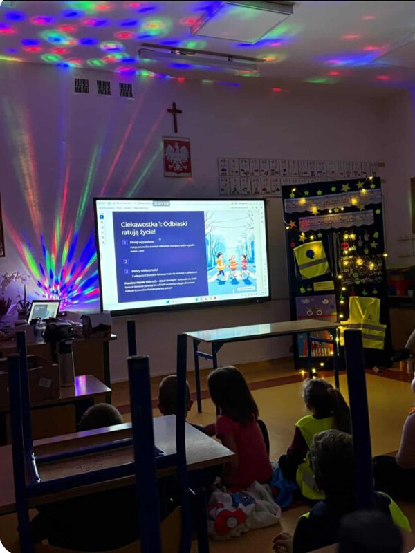 Uczniowie w kamizelkach słuchają prezentacji o odblaskach