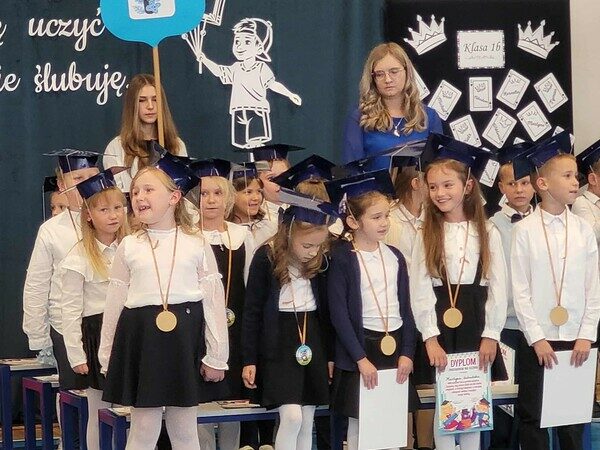 Grupa dzieci z klasy 1b stoi i śpiewa piosenkę