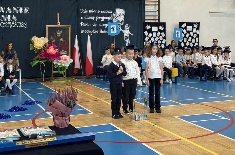 trzech uczniów stoi na środku sali i recytują wiersze
