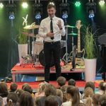 mężczyzna stoi na scenie przed grupą dzieci