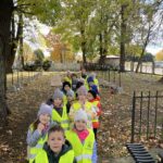 Uczniowie ubrani w kamizelki odblaskowe stoją na cmentarzu