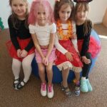 Cztery dzieweczynki siedzą na dużej pufie w strojach postaci z bajek