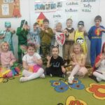 Dziewięcioro dzieci stoi, pięcioro dzieci siedzi przed nimi na dywanie wszystkie dzieci są w strojach postaci z bajek