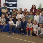 Grupa dzieci pozuje do zdjęcia po pasowaniu na czytelnika, z tyłu po prawej stronie stoją dwie panie i po lewej stoją dwie panie.