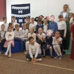 Grupa dzieci pozuje po zdjęcia, z tyłu z prawej strony stoi pani.