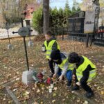 Trzech chłopców pochyla się nad grobem i stawiają znicz.