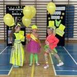 Trzy dziewczynki prezentują swoje stroje odblaskowe, każda z nich trzyma balony.