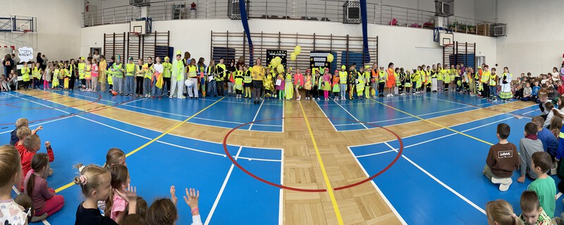 Dzieci ubrane w stroje odblaskowe stoją na sali gimnastycznej.