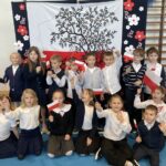 Grupa dzieci z horągiewkami w dłoniach stoją na tle dekoracji patriotycznej.