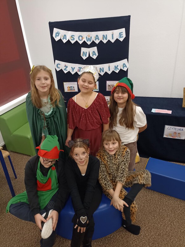 W pierwszym rzędzie od lewej strony siedzi chłopiec przebrany za elfa, obok siedzą dwie dziewczynki przebrane za koty. Z tyłu stoją trzy dziewczynki przebrane w baśniowe stroje.