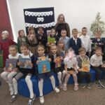 Grupa dzieci pozuje do zdjęcia po pasowaniu na czytelnika, z tyłu za dziećmi stoi pani.