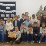 Grupa dzieci pozuje do zdjęcia po pasowaniu na czytelnika, z tyłu z prawej strony stoi pani.