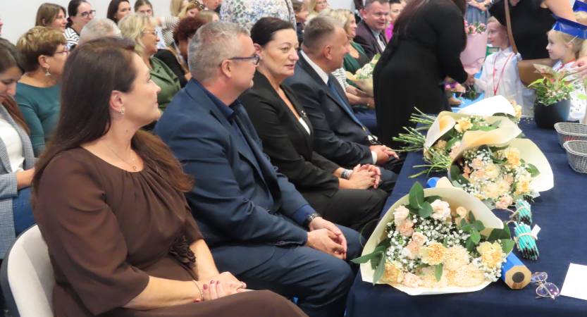 Zaproszeni goście siedzą przy stole, na którym leżą kwiaty